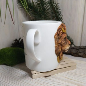 May include: White ceramic mug with a 3D sculpted lion head on the side. The lion has a golden crown and brown fur.