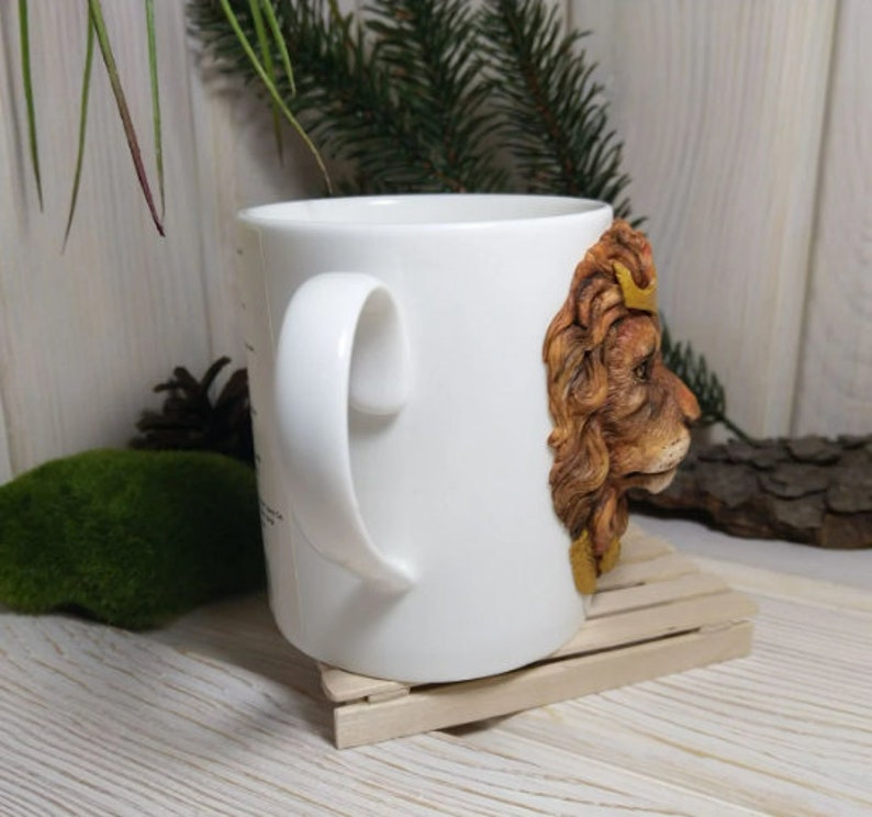 May include: White ceramic mug with a 3D sculpted lion head on the side. The lion has a golden crown and brown fur.