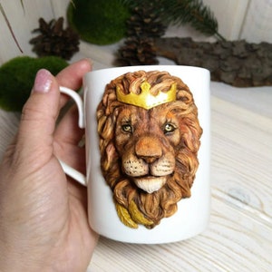 May include: White ceramic mug with a 3D sculpted lion's head wearing a gold crown. The lion has a brown mane and a realistic expression.