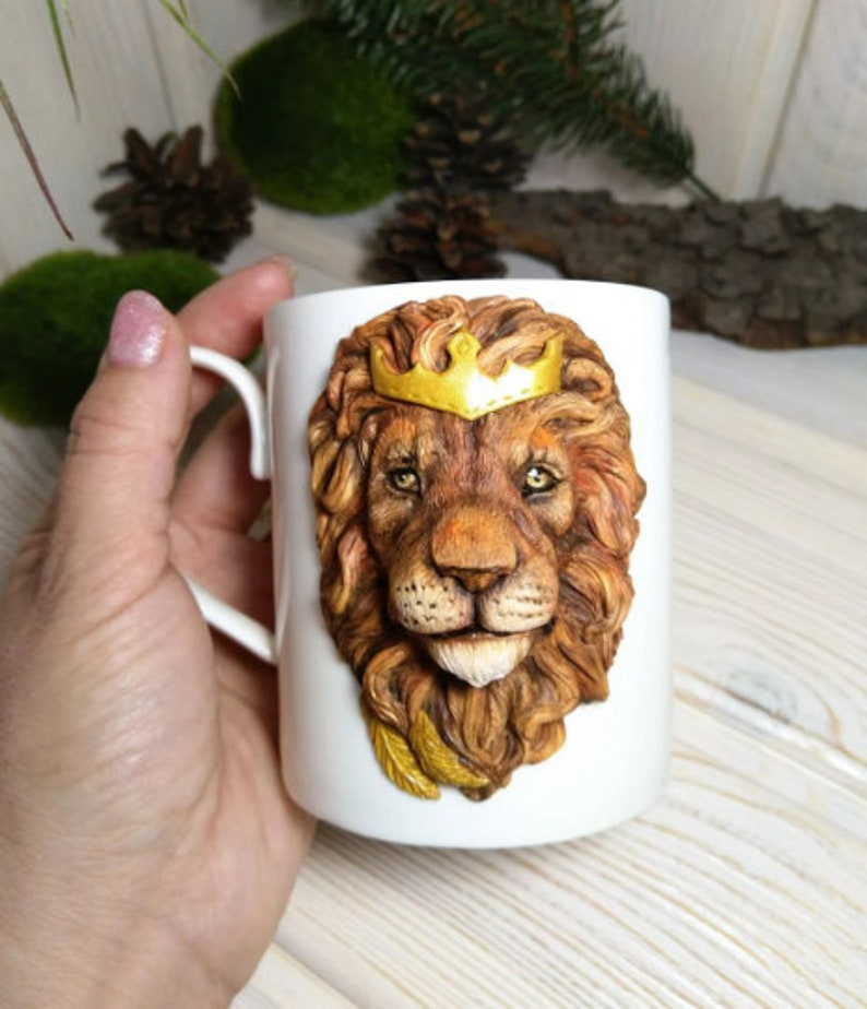 May include: White ceramic mug with a 3D sculpted lion's head wearing a gold crown. The lion has a brown mane and a realistic expression.
