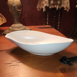 May include: A white oval-shaped ceramic serving bowl on a wooden table.
