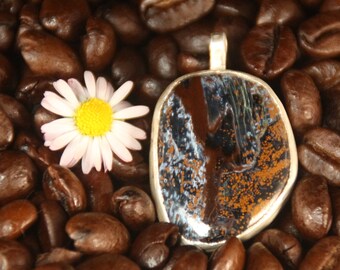 May include: A silver pendant with a brown, blue, and white agate stone set in a silver bezel. The pendant is surrounded by coffee beans.