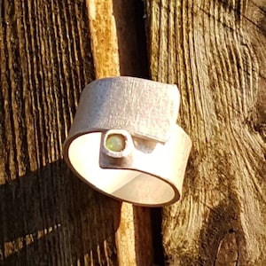 Könnte beinhalten: Ein silberner Ring mit einem grünen Edelstein in der Mitte. Der Ring ist verdreht und hat ein einzigartiges Design.
