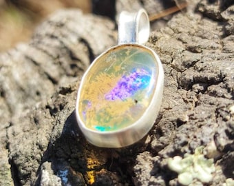 May include: A silver pendant with a yellow, iridescent opal stone. The stone has a purple and blue flash.