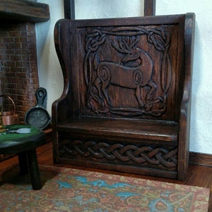 May include: A dark brown wooden bench with a carved deer design and Celtic knotwork. The bench has a high back and a seat with a small shelf underneath.