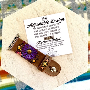 May include: Brown leather watch band with a purple flower design and silver hardware. The band features a decorative floral pattern with yellow and pink accents. A card with text about the adjustable design is also visible.