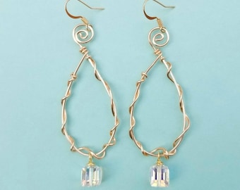 May include: A pair of gold-toned wire earrings. The earrings feature a teardrop shape with a twisted wire design and a small, iridescent, cube-shaped charm at the bottom. The top has a spiral design and a hook for the ear.