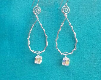 May include: A pair of silver-toned wire earrings. Each earring features a teardrop shape with a spiral at the top and a wrapped wire design. A small, iridescent cube-shaped crystal hangs from the bottom of each earring.