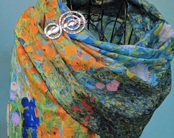 May include: A colorful scarf with a floral design in shades of orange, yellow, blue, and green is draped over a black metal form. A silver brooch with a swirling design secures the scarf.