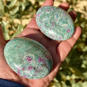 May include: Two green and pink tumbled stones with a speckled pattern. The stones are smooth and polished.