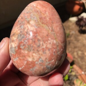 May include: A smooth, polished egg-shaped stone with a pink, white, and gray marbled pattern.
