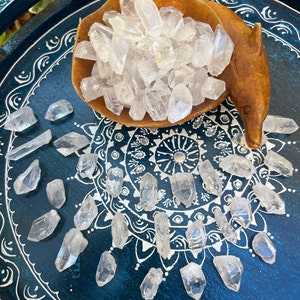 May include: A wooden bowl filled with clear quartz crystal points, surrounded by more points on a blue and white patterned surface.