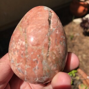 May include: A smooth, polished, pink and white egg-shaped stone with visible veins and striations.