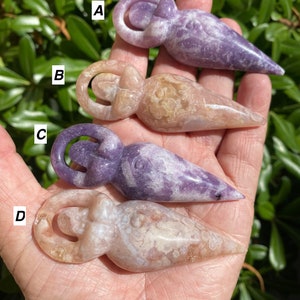 May include: Four carved crystal figurines in the shape of a woman. The figurines are made of amethyst and agate and have a purple, white, and brown color scheme.