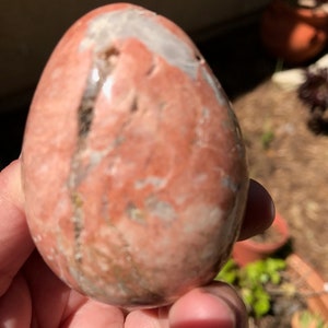 May include: A smooth, polished, egg-shaped stone with a pink, white, and brown marbled pattern.