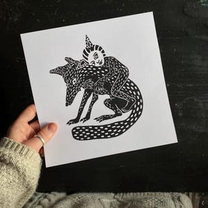 Peut inclure: Estampe en linogravure en noir et blanc représentant une figure chevauchant un renard. Le renard et le cavalier sont recouverts de motifs pointillés. Le cavalier porte une coiffe pointue. L'œuvre est sur papier blanc.