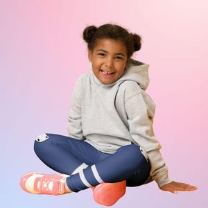 Puede incluir: Una persona joven con una sudadera con capucha gris, leggings azul marino con rayas blancas y zapatillas rosas. La persona est&aacute; sentada con las piernas cruzadas y sonriendo, con un fondo degradado colorido de rosa, morado y azul.