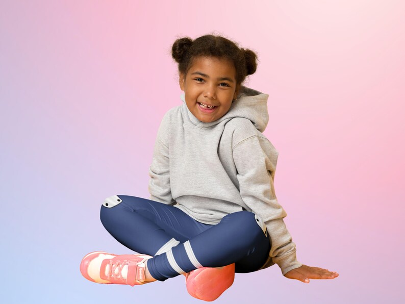 Puede incluir: Una persona joven con una sudadera con capucha gris, leggings azul marino con rayas blancas y zapatillas rosas. La persona est&aacute; sentada con las piernas cruzadas y sonriendo, con un fondo degradado colorido de rosa, morado y azul.