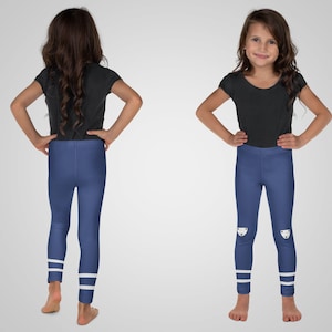 Puede incluir: Una ni&ntilde;a peque&ntilde;a lleva una camiseta negra de manga corta y leggings azules. Los leggings tienen rayas blancas en los tobillos y un gr&aacute;fico blanco en las rodillas. La ni&ntilde;a est&aacute; de pie con las manos en las caderas.