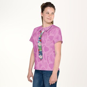 A young woman wearing a pink shirt with a tie pattern and smiling at the camera.