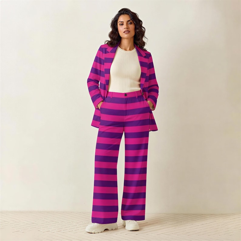 A woman wearing a purple and pink striped suit and white top stands in front of a white wall.