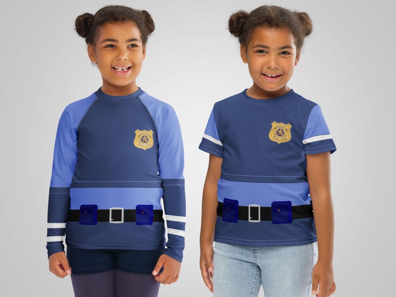 Puede incluir: Dos ni&ntilde;os con disfraces de polic&iacute;a azules. Los trajes presentan una insignia, un cintur&oacute;n con hebilla plateada y una franja azul claro en el pecho. Uno tiene mangas largas, el otro mangas cortas.