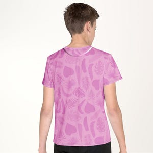 A person wearing a pink t-shirt with a pattern of leaves and hearts on it.