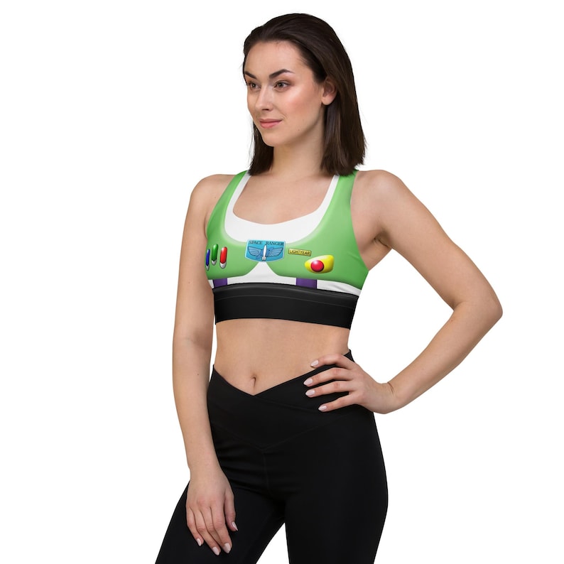 A woman wearing a green and white sports bra with colorful buttons and a red button on the front, posing confidently with her hands on her hips.