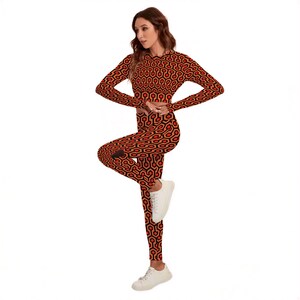 A woman wearing a leotard with a geometric pattern in red and orange colors, posing with her hands on her hips.