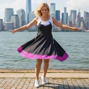 May include: A black and white dress with a pink and purple hem, featuring a spiderweb design. The dress has a white top with a geometric design. The background shows a cityscape and water.