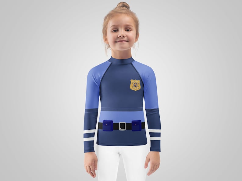 Puede incluir: Una camisa azul y azul claro de manga larga con un dise&ntilde;o de insignia de polic&iacute;a. La camisa presenta un cintur&oacute;n simulado con un cintur&oacute;n negro y una hebilla plateada, y pantalones blancos. La camisa est&aacute; dise&ntilde;ada para parecer un uniforme de polic&iacute;a.