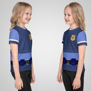 Puede incluir: Dos camisetas infantiles dise&ntilde;adas para parecer un uniforme de polic&iacute;a. Las camisetas son principalmente azul marino con detalles en azul claro, una insignia dorada y un dise&ntilde;o de cintur&oacute;n negro con bolsas azules. Las mangas tienen rayas blancas.