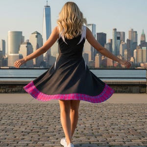 May include: A black dress with white accents and a pink and purple hemline. The dress has a flared skirt and is sleeveless. The background features a cityscape with tall buildings and a body of water.