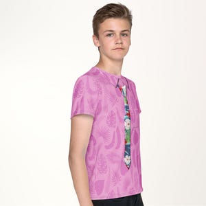 A young boy wearing a pink t-shirt with a colorful tie printed on it, posing for a portrait against a plain white background.