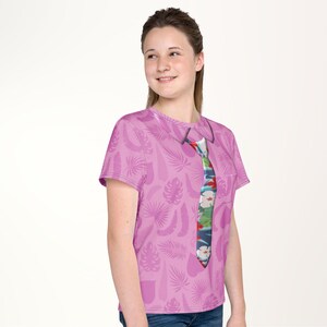 A young woman wearing a pink t-shirt with a colorful tie printed on it, smiling at the camera.