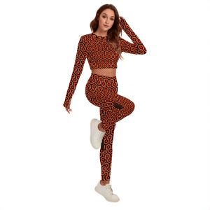 A woman wearing a red and orange patterned outfit, including a crop top and leggings, posing with one leg on the ground and the other leg lifted in the air.