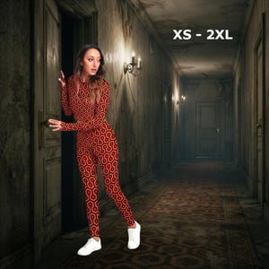 A woman in a red and orange patterned outfit stands in a dimly lit hallway, with a doorway visible in the background.
