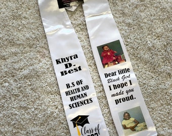 May include: White graduation sash with black text and images. The text reads "Khyra D. Best B.S. of Health and Human Sciences Class of 2022" and "Dear little Black Girl I hope I made you proud."