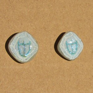 May include: A pair of white ceramic earrings with a blue and white design. The design is a stylized image of a bird.