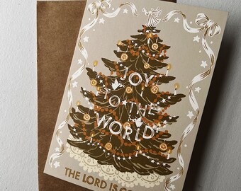 May include: A Christmas card with a brown envelope. The card features a stylized illustration of a Christmas tree decorated with ornaments, candles, and the text "Joy to the World! The Lord is Come!"