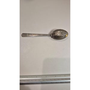 May include: A silver tea infuser with a long handle and a perforated oval-shaped bowl. The handle has decorative etchings near the top. The infuser is designed for steeping loose leaf tea.