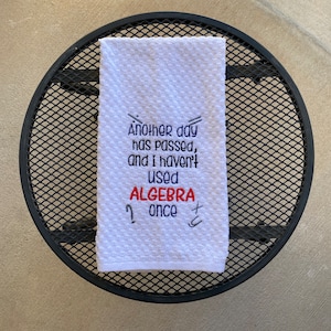 May include: White kitchen towel with embroidered text that reads "Another day has passed, and I haven't used ALGEBRA once".