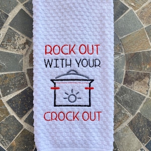 May include: White kitchen towel with a textured pattern. The towel features the embroidered phrase "ROCK OUT WITH YOUR CROCK OUT" in red and black thread, along with a graphic of a slow cooker.
