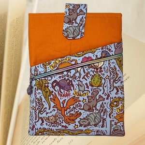 May include: A blue and orange fabric zippered pouch with a whimsical design featuring various creatures from the Harry Potter universe, including a phoenix, a spider, a three-headed dog, and a cat. The pouch has a zipper closure and a flap with a button closure.