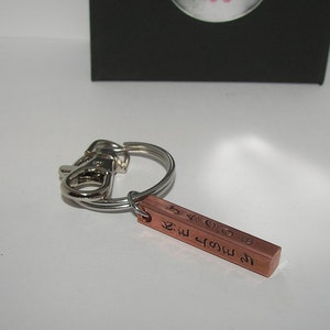 May include: A silver key chain with a copper bar charm. The charm has the text "We grow old together" engraved on it.