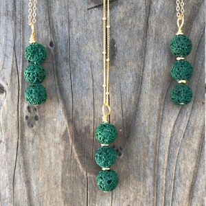 May include: Three necklaces with green lava rock beads and gold chains. The necklaces are hanging on a wooden surface.