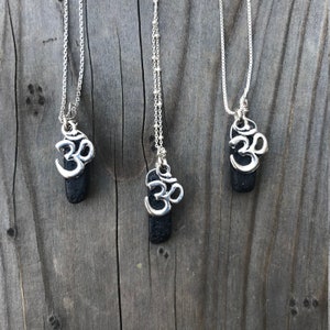Peut inclure: Trois colliers en argent avec des pendentifs en pierre de lave noire ornés d'un symbole Om en argent.