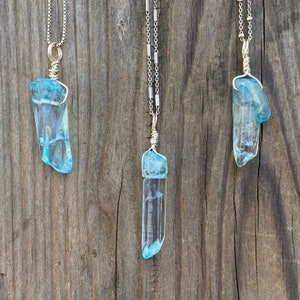 Puede incluir: Tres collares de plata con colgantes de cristal azul. Los cristales son largos y delgados, parecidos a fragmentos de hielo.