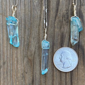 Puede incluir: Tres collares de plata con colgantes de cristal azul. Los colgantes est&aacute;n envueltos en alambre de plata y son de diferentes tama&ntilde;os. Los collares est&aacute;n colgados en una superficie de madera.