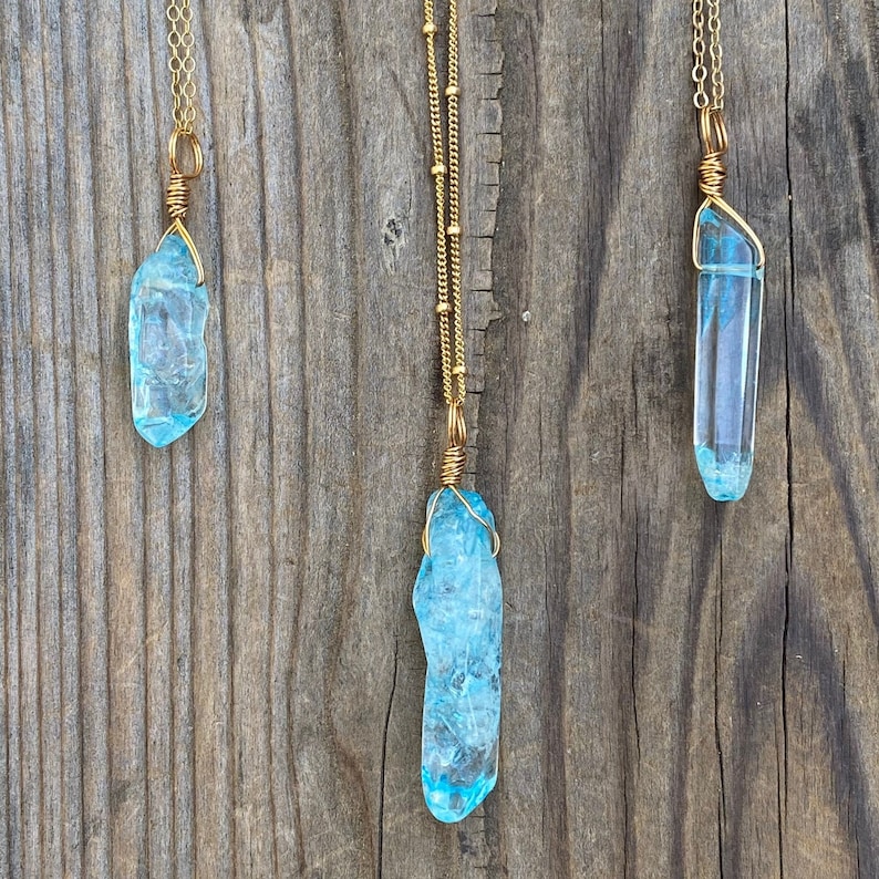 Puede incluir: Tres collares de oro con colgantes de cristal azul. Los cristales est&aacute;n envueltos en alambre de oro y tienen un aspecto crudo y natural.